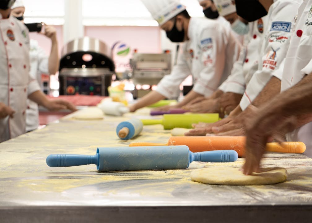 Which Baking Course Is Right for You? Workshops, Short Courses, and Diplomas Compared (2026) 6 Culinary school students in white chef uniforms rolling dough together in a professional baking class.