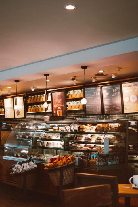 A bright, modern café interior in Ahmedabad with wooden furniture, pendant lights, and a chalkboard menu on the wall.