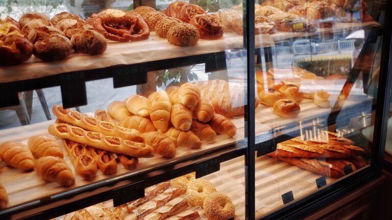 A well-stocked bakery display case filled with fresh breads, croissants, and pastries arranged on wooden shelves