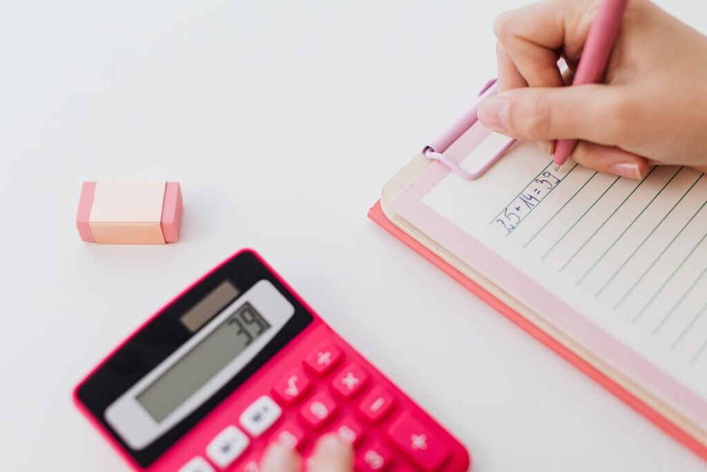 How to Price Your Baked Goods: The Complete Formula for Home Bakers in India (2026) 3 A person writing pricing calculations in a notebook next to a calculator, representing home baker cost planning.