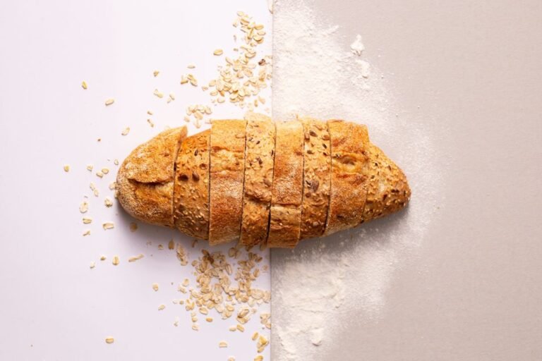 A freshly baked rustic sourdough loaf with a scored crust resting on a wooden board in a bright kitchen.
