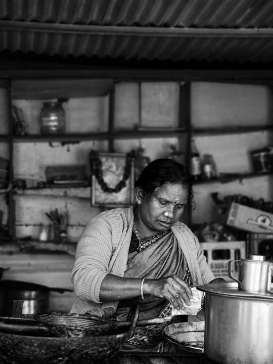 A South Asian woman preparing food in a traditional Indian kitchen, representing authentic Jain home cooking in Ahmedabad.