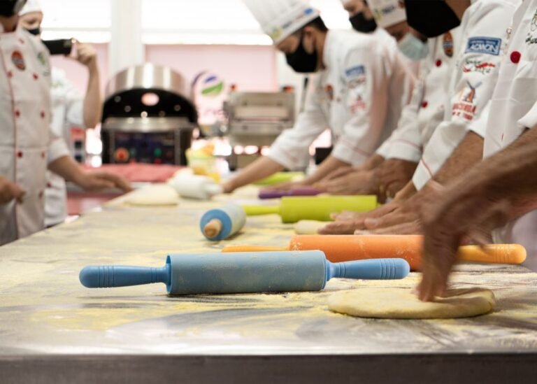 Culinary school students in white chef uniforms rolling dough together in a professional baking class.