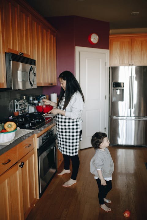 A mother and young child cooking together in a warm home kitchen, preparing a healthy vegetarian meal.