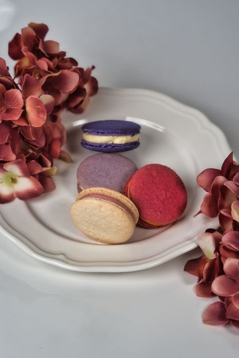 Close-up of vibrant French macarons with smooth shells and perfect ruffled feet arranged on a white plate.