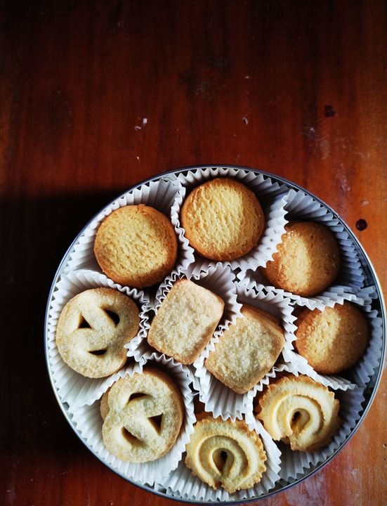 Assorted Danish-style butter cookies arranged neatly in a round tin box on a wooden table.