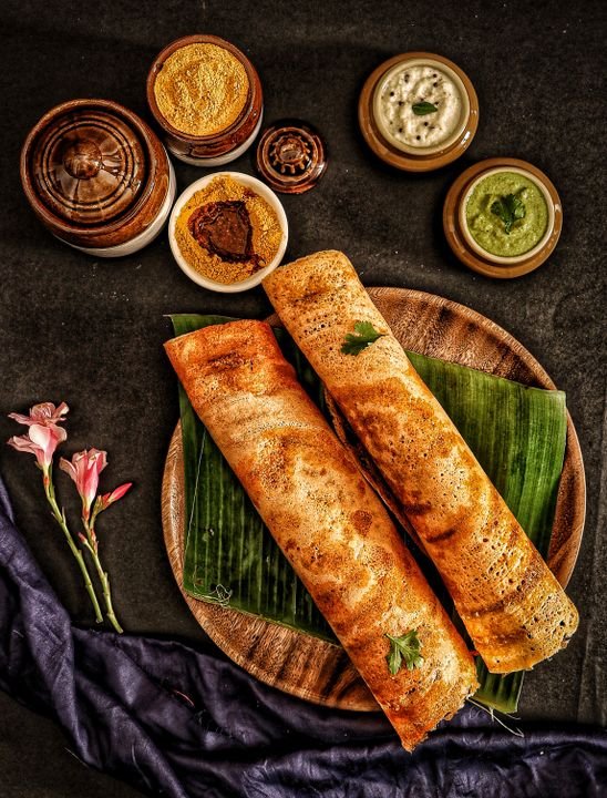 A traditional Indian thali served on a round steel plate with multiple small bowls of colourful curries, dal, rice, flatbreads, and accompaniments arranged around the plate.