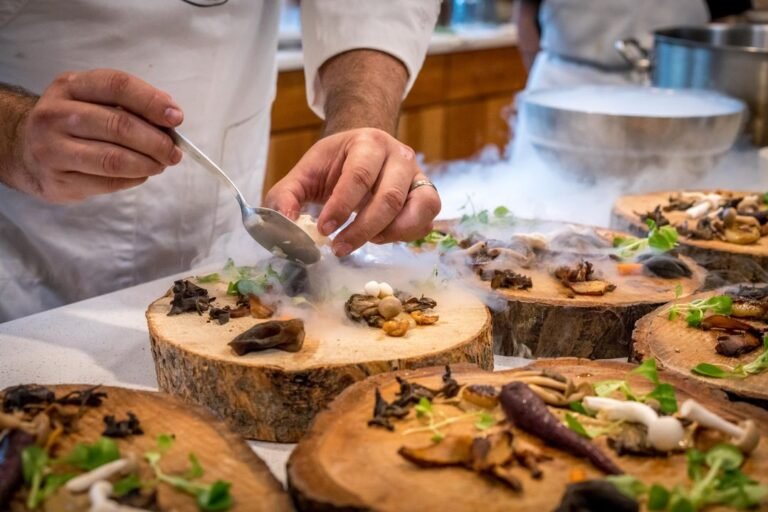 A chef carefully plates a vibrant vegetarian Indian dish on a wooden surface, with golden curries and fresh herbs arranged in a colourful composition.