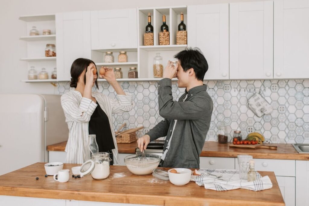 Home Bakery Equipment: What You Actually Need to Start (Under ₹15,000) 9 Two people baking together in a bright home kitchen, mixing batter in a bowl surrounded by baking tools and ingredients, representing affordable home bakery setup in India.