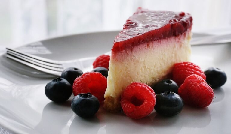 Perfect smooth cheesecake slice on a white plate with berry topping