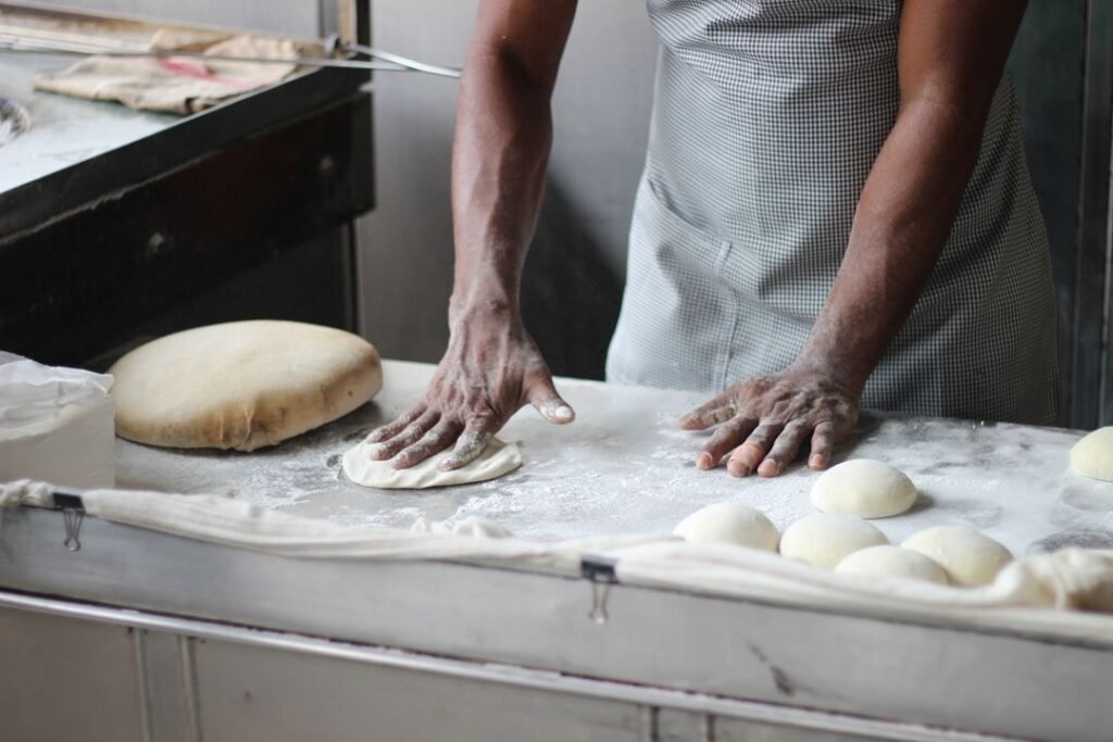 7 A culinary student kneading bread dough at a professional kitchen worktop, demonstrating hands-on practical training.