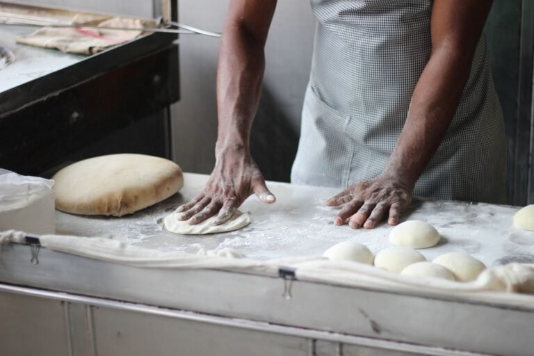 A culinary student kneading bread dough at a professional kitchen worktop, demonstrating hands-on practical training.