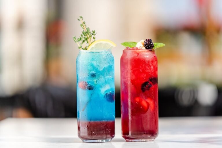 Vibrant colourful mocktails garnished with berries, mint, and lemon slices arranged on a sunny café table.
