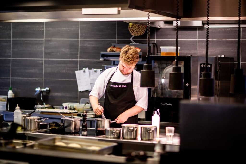 How to Open a Cloud Kitchen in Ahmedabad: Licences, Cost, and Setup Guide 2026 1 A professional commercial kitchen with stainless steel counters, industrial burners, and a chef plating food for delivery orders in Ahmedabad.