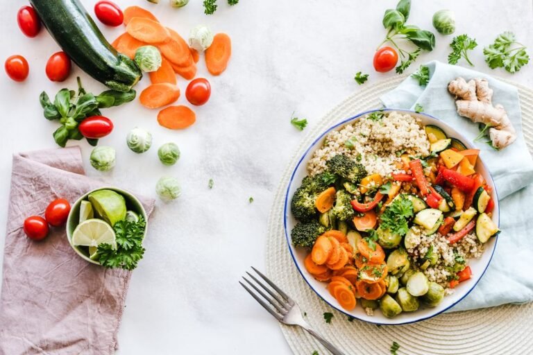 A vibrant, colorful salad bowl filled with fresh vegetables, chickpeas, and greens arranged on a wooden table in natural light.