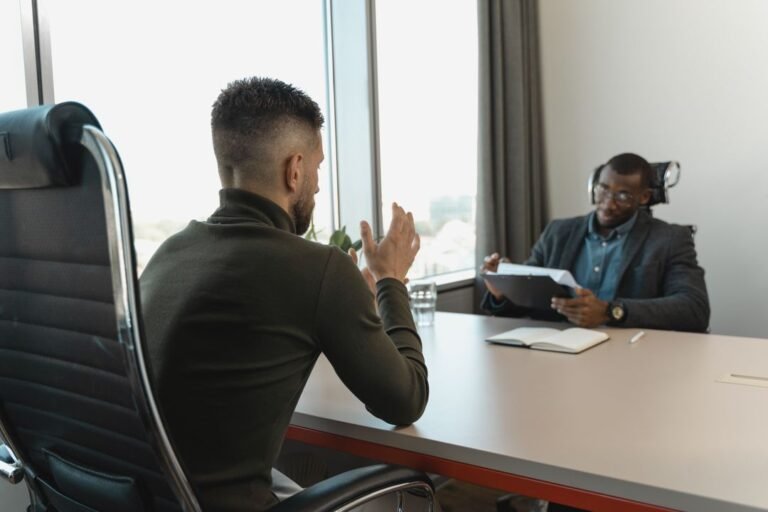 Two men in a formal interview setting in a modern office with large windows