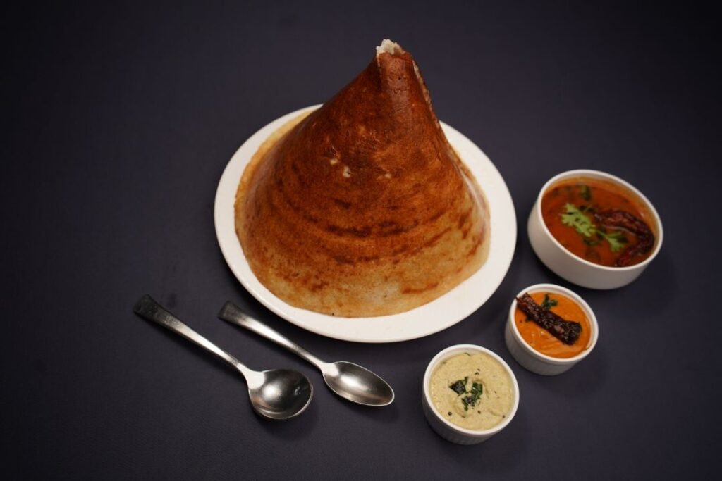 Crispy cone dosa served with authentic Indian chutneys and sambar on a dark backdrop