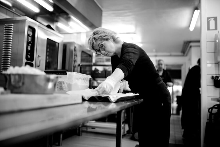 A woman chef working with focus at a stainless steel prep table in a professional restaurant kitchen.