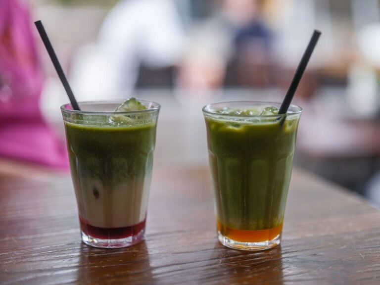 Two iced matcha lattes in tall glasses, layered green and white, served cold.
