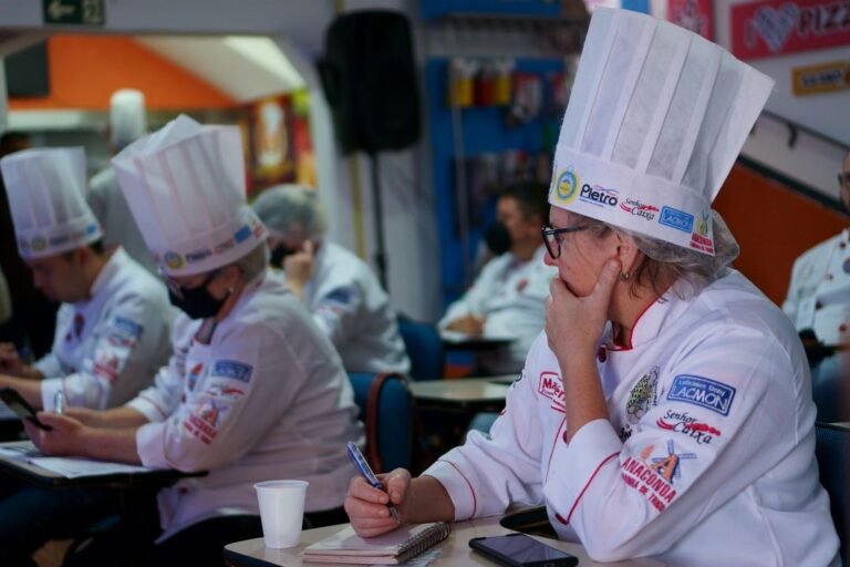 A group of culinary students in chef whites taking notes during a professional cookery class.