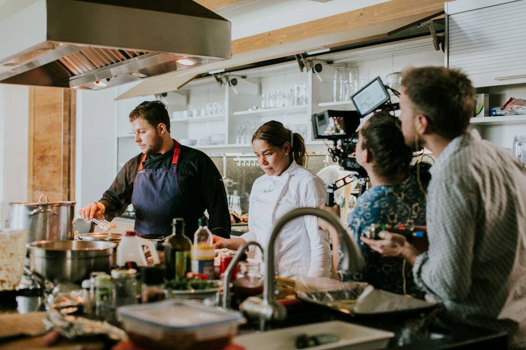 A food production team filming a cooking shoot in a bright test kitchen, the working environment of a professional recipe developer.