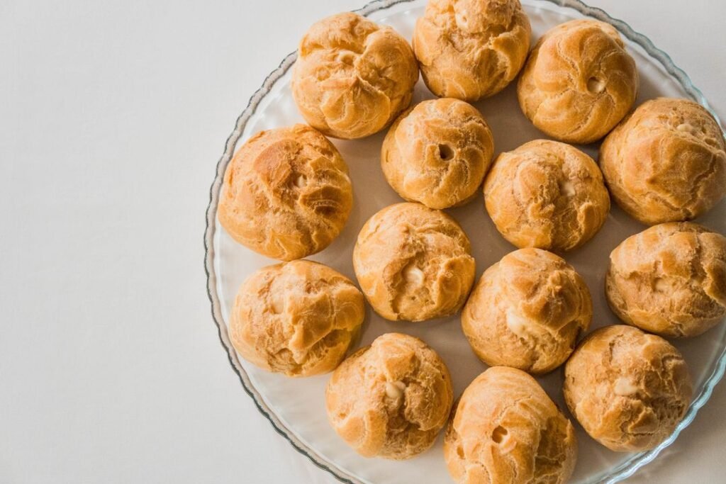 A tray of golden baked cream puffs arranged on a glass plate, the classic result of well-made choux pastry.