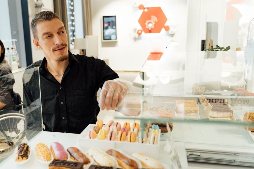 French Macaron Troubleshooting: Why They Crack, Stay Hollow, or Weep 1 A pastry chef carefully arranging rows of macarons and eclairs on a bakery counter.