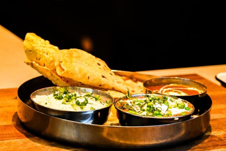 An Indian thali served with rice, paneer curry and fresh flatbread on a wooden table.