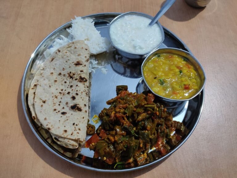 A steel thali of chapati, rice, dal, curd and bhindi sabzi - a Jain-friendly meal made without root vegetables.