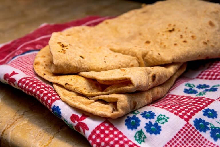A freshly cooked chapati resting on a patterned cloth, showing the soft puffed texture of well-made roti.
