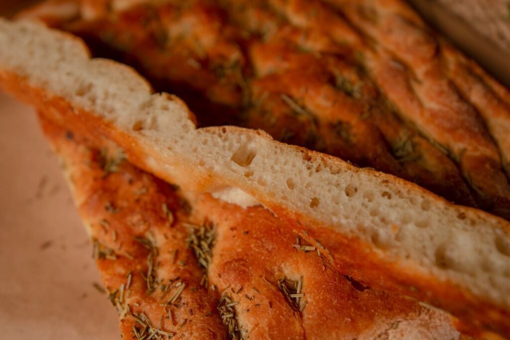Sliced rosemary focaccia bread showing its airy, open crumb studded with herbs.