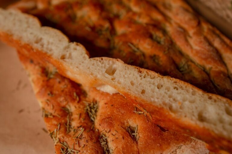 Sliced rosemary focaccia bread showing its airy, open crumb studded with herbs.