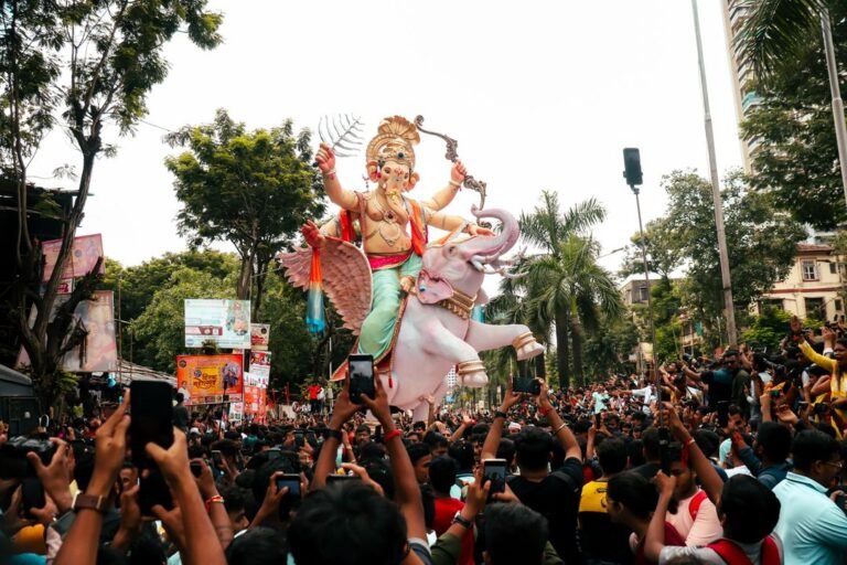 A large decorated Ganesha idol carried through a crowded street procession during Ganesh Chaturthi.
