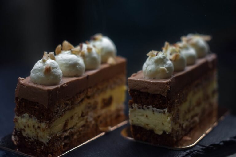 A cross-section slice of a layered mousse entremet cake showing sponge, cream, and chocolate mousse layers, piped on top.