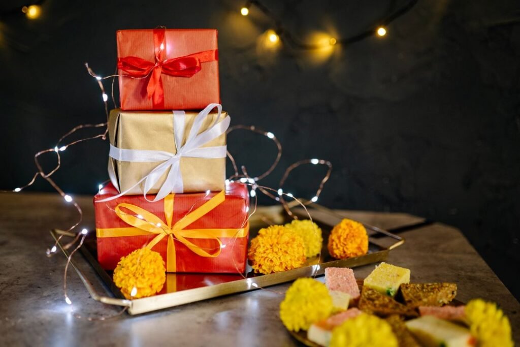 Corporate Diwali Gifting: How Home Bakers Win Bulk B2B Orders (Quotes, Samples, GST Invoices) 4 Three stacked red and gold wrapped Diwali gift boxes on a brass tray with marigolds, fairy lights and a plate of Indian sweets.
